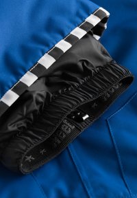 Blått tyg med svart elastisk kant, med ett vitt och svart randigt accent. Slen textur med en rynkad sektion och knappdetaljer.