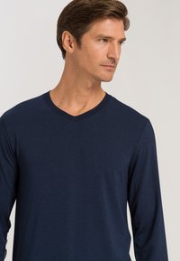 Maglietta a maniche lunghe di colore blu navy con scollo a V e texture liscia. Design semplice senza motivi o accenti.