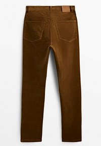 Pantalon en velours côtelé marron avec poches arrière, passants de ceinture et un patch de marque en cuir sur la ceinture, posé à plat sur un fond blanc.