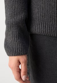 Ciemnoszary sweter z dzianiny, rękaw z prążkowanym wzorem, wąski mankiet, prezentujący miękką, grubą przędzę i subtelne różnice w kolorze.