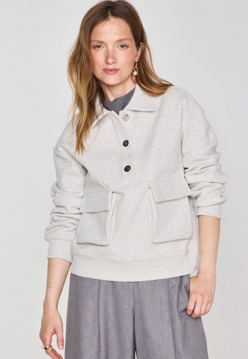 Sweatshirt gris clair avec col, doté d'une fermeture à boutons, de poches avant et d'une texture douce, associé à un pantalon gris.