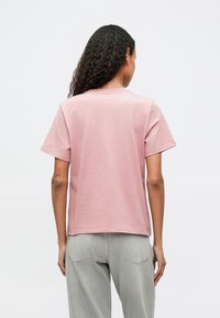 Ροζ ανοιχτό κοντομάνικο μπλουζάκι με στρογγυλή λαιμόκοψη, φτιαγμένο από απαλό βαμβάκι, με απλό σχέδιο και χαλαρή εφαρμογή. Η πίσω όψη δεν έχει διακοσμήσεις.