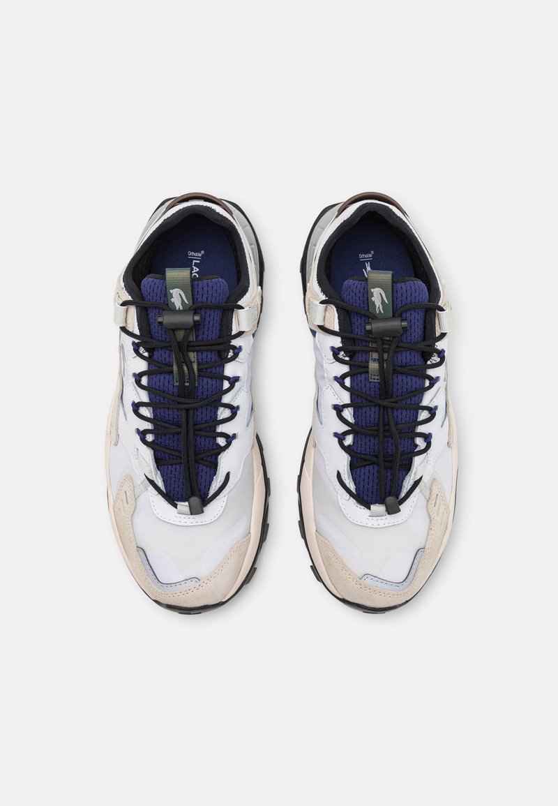 Un paio di sneakers bianche, beige e blu navy con lacci neri e un'etichetta verde, viste dall'alto su uno sfondo bianco.