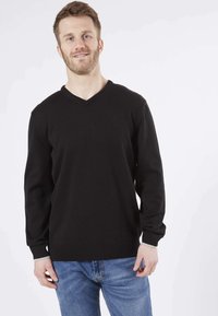 Pull noir en V en matière douce, avec des poignets et un ourlet côtelés, associé à un jean en denim bleu clair.