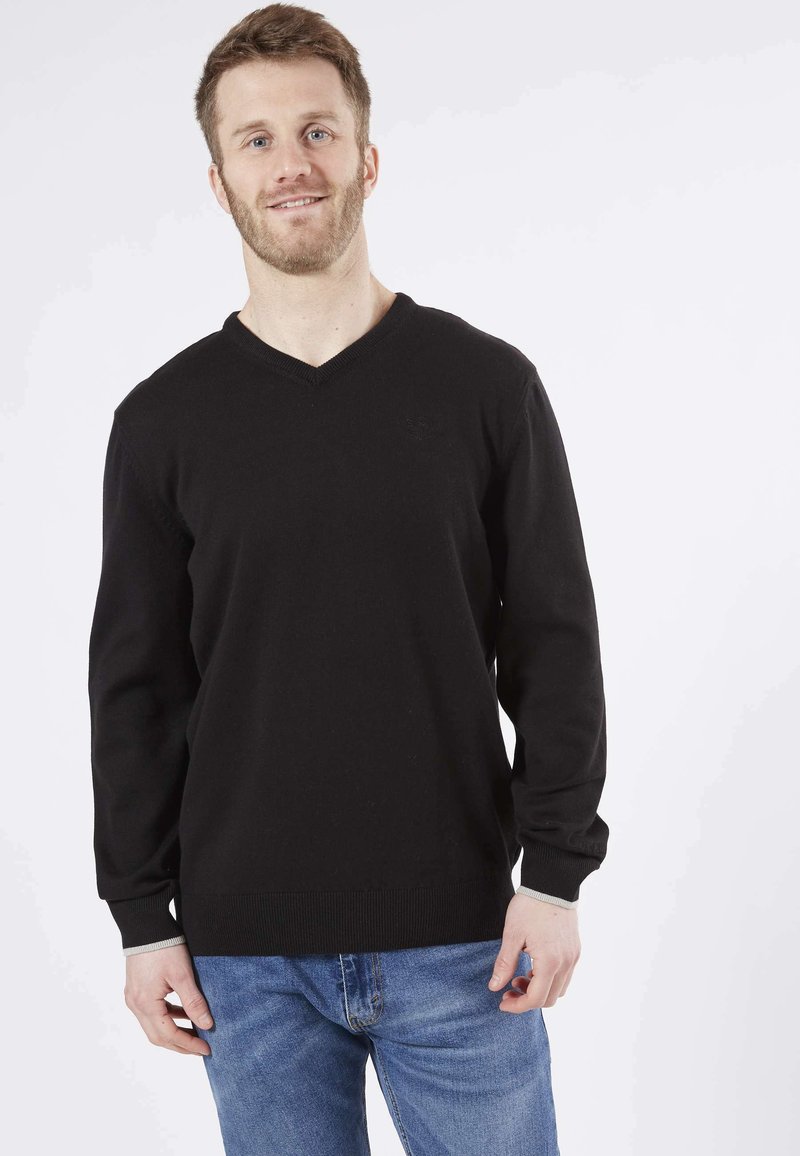 Pull noir en V en matière douce, avec des poignets et un ourlet côtelés, associé à un jean en denim bleu clair.