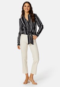 Zwart-witte gestreepte blouse met een gestrikte voorkant, gecombineerd met crème rechte broek en doorzichtige hakken mules.