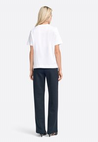 White short-sleeve t-shirt with a round neckline, paired with dark, wide-leg pants and black heeled shoes. Simple, clean design.