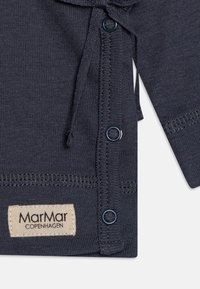 Tengerész kék kötött ruházat, zsinórral, kék gombokkal és varrt díszítéssel. Tartalmaz egy textil címkét, amelyen szerepel a "MarMar COPENHAGEN" felirat.