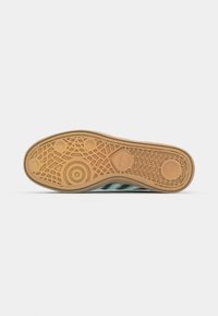 Semelle de chaussure de sport verte avec un fond en caoutchouc gomme texturé, présentant un motif géométrique et des accents circulaires.
