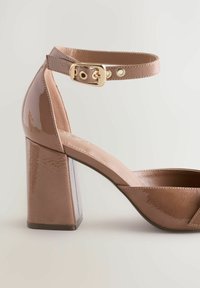 Brown patent heeled sandal with a thick block heel, open toe, adjustable ankle strap with gold buckle, and smooth textured upper.
