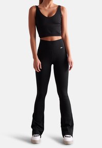 Top corto negro de canalé con tirantes anchos combinado con leggings negros acampanados; ambos hechos de una tela elástica. Detalle del logotipo en blanco en los leggings.
