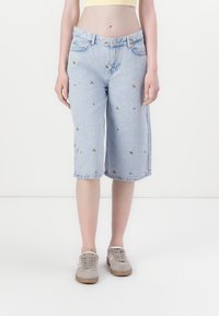 Bermudas en jean bleu clair avec broderies florales, taille mi-haute et ourlet roulé. Comprend des passants de ceinture et deux poches avant.