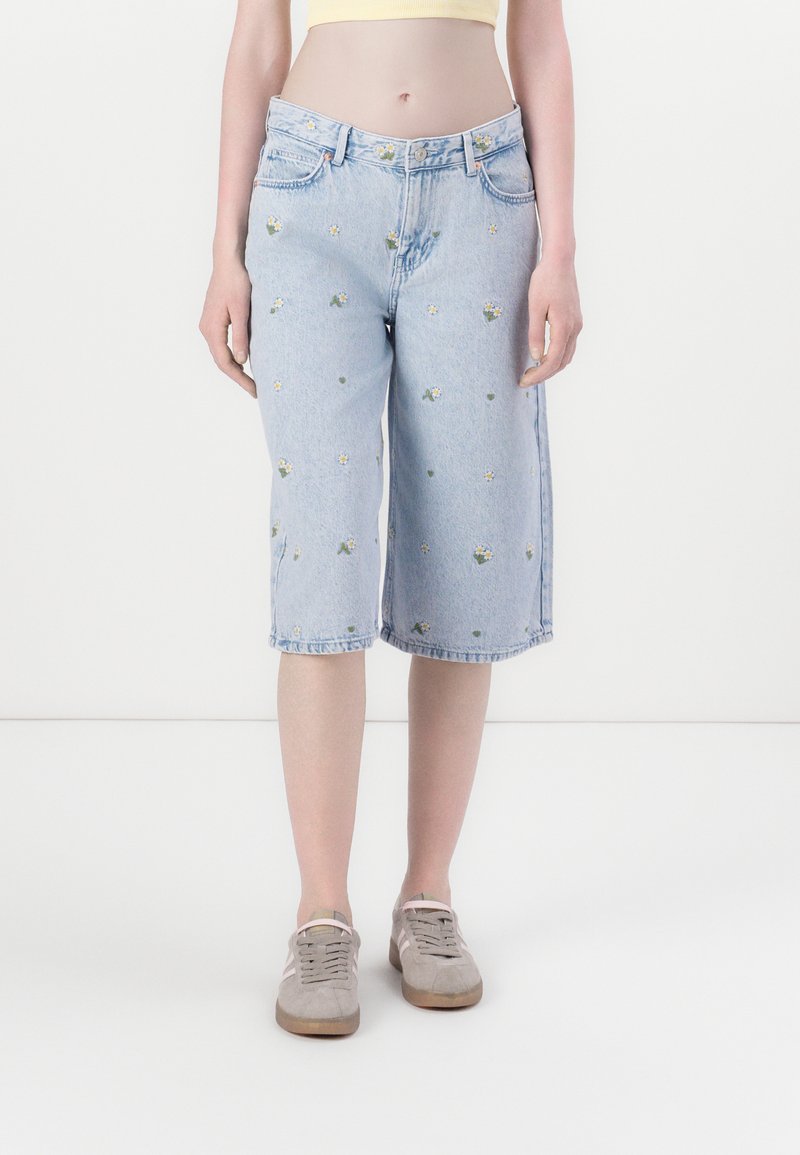Bermudas en jean bleu clair avec broderies florales, taille mi-haute et ourlet roulé. Comprend des passants de ceinture et deux poches avant.