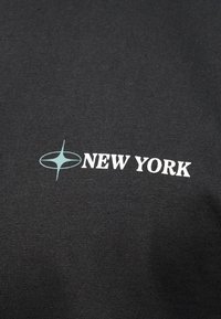 Μαύρο ύφασμα με λευκό κείμενο "NEW YORK" και ανοιχτό μπλε αστέρι αριστερά του κειμένου.