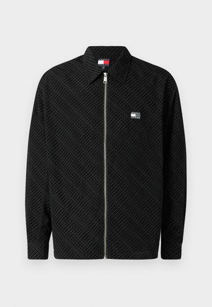 Crna jakna na zip s teksturiranim uzorkom. Ima ovratnik i mali logotip na lijevoj strani prsnog dijela. Dugi rukavi ravnog kroja.
