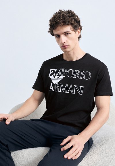 Μαύρο βαμβακερό t-shirt με λευκό κείμενο και λογότυπο "EMPORIO ARMANI". Κλασικός στρογγυλός λαιμός, κοντά μανίκια και εφαρμοστή σιλουέτα.