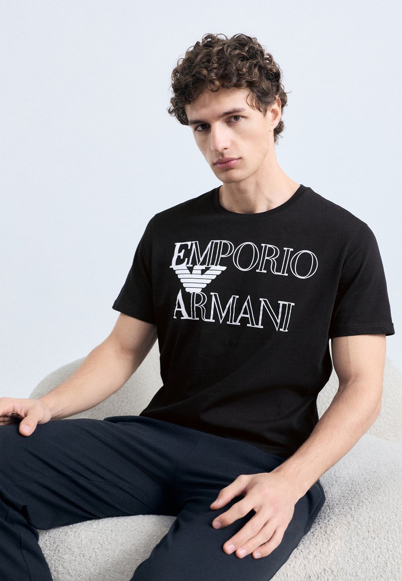 Čierne bavlnené tričko s bielym nápisom a logom "EMPORIO ARMANI". Klasický okrúhly výstrih, krátke rukávy a priliehavý strih.
