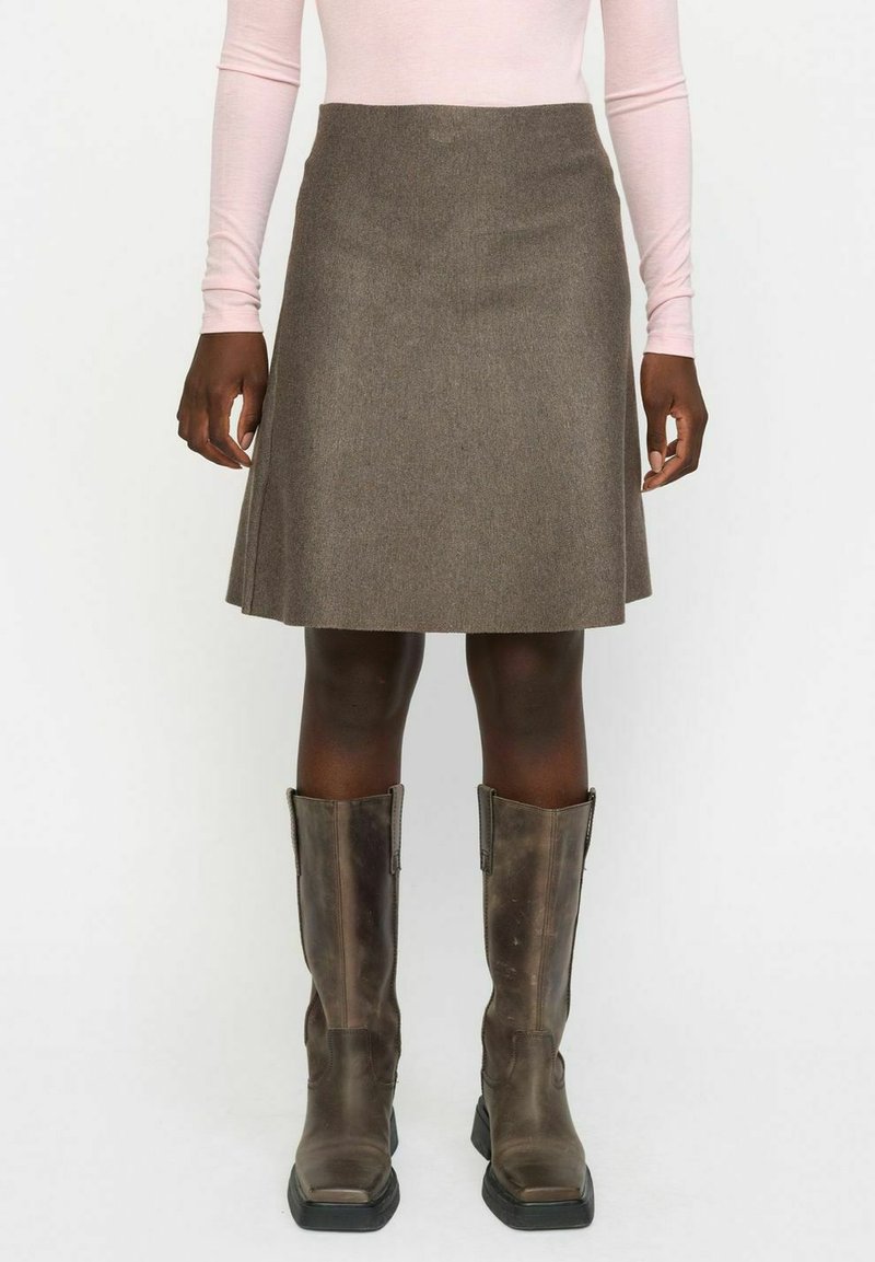 Jupe en laine marron au design évasé, tombant au-dessus du genou, associée à des bottes en cuir marron montantes. Un haut rose à manches longues est visible.