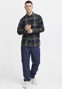 Camisa de botones en un patrón a cuadros verde oscuro y marino, hecha de algodón. Combinada con pantalones holgados marinos y zapatillas blancas.