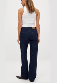 Jeans de tiro alto en denim de color azul oscuro y corte ancho, con bolsillos traseros y una pequeña etiqueta de marca en beige en la cintura.