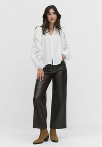Weißes Hemdblusenshirt mit puffigen Ärmeln und Spitze. Kombiniert mit hochgeschnittenen, braunen Fake-Leder-Hosen mit weitem Bein und hellbraunen Ankle-Boots.