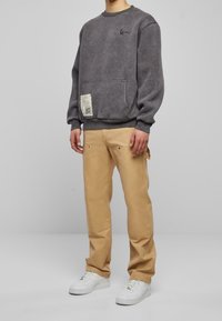 Šedá mikina s kapsou a potiskem, v kombinaci s béžovými kalhotami. Bílé tenisky tvoří dokonalý outfit. Jednoduchý, ležérní design.