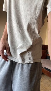 Inimene, kes kannab helehallikat, kergelt kortsus t-särki ning tumedamat halli dressipükse, seisab toas diivani ja parkettpõranda lähedal.