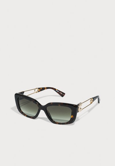 Ochelari de soare cu tartan, cu un cadru pătrat, lentile cu gradient verde și accente din metal de culoare aurie pe brațe.