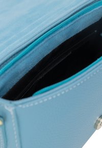 Borsa a mano in pelle azzurro chiaro con superficie texture, dotata di chiusura con zip e foderatura turchese a contrasto. Tasca interna in tessuto nero.