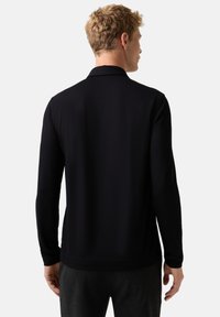 Schwarzes Poloshirt mit langen Ärmeln, glatter Textur und Standardkragen. Es zeichnet sich durch einen geraden Schnitt und gerippte Bündchen aus.