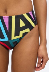 Γυναίκα που φοράει πολύχρωμα κάτω μέρος μπικίνι με μεγάλα γράμματα σε μπλε, κόκκινο, ροζ, κίτρινο και μαύρο σε λευκό φόντο.