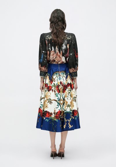 Naine seisab seljaga, seljas must pikkade varrukatega pluus klassikalise maaliga ja sinise lillemustriga midi-seelik.