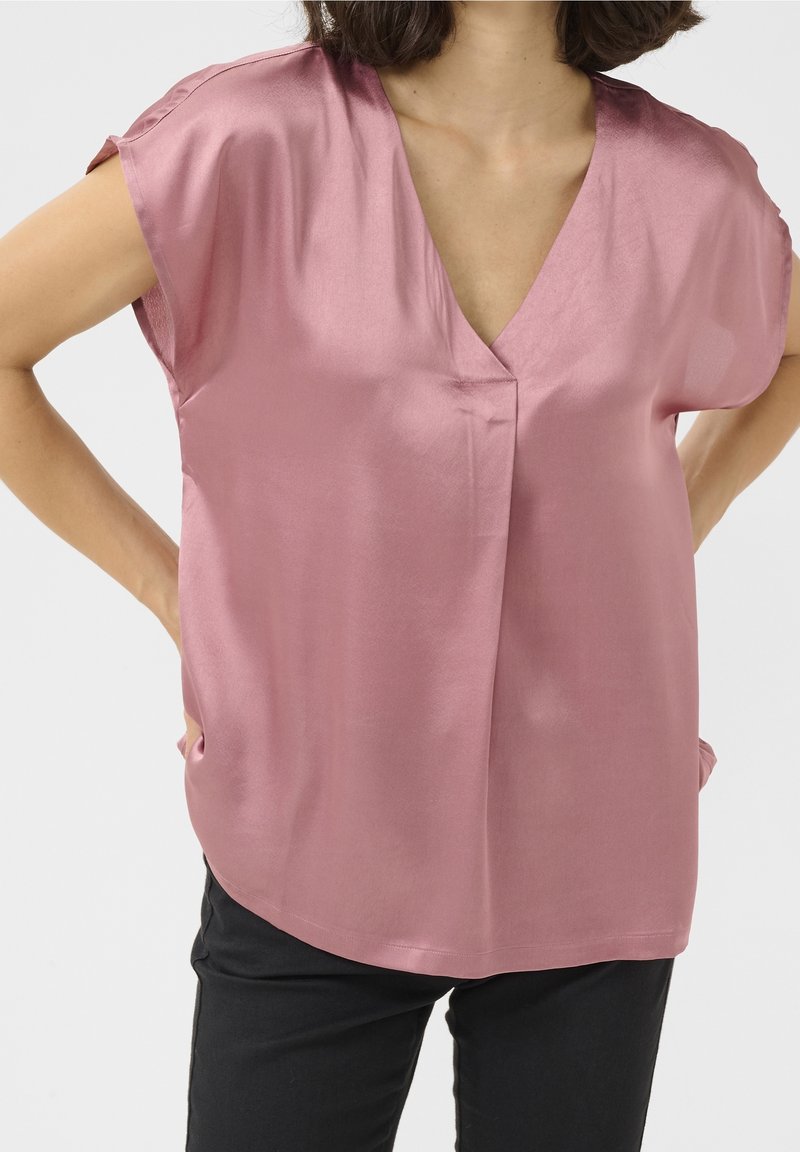 Blouse à manches courtes et col en V, fabriquée en satin rose lisse, avec une coupe décontractée et des poches latérales dotées de détails de couture subtils.