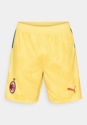 Żółte spodenki sportowe z logo AC Milan na lewej nodze i czerwonym logo Puma na prawej nodze, z subtelnym geometrycznym wzorem i elastycznym pasem.