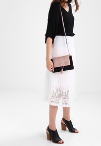 Top nero a coste con scollo a V, gonna bianca plissettata con bordatura in pizzo, tacchi aperti neri e borsa a tracolla rosa e nera con dettaglio di nappine.