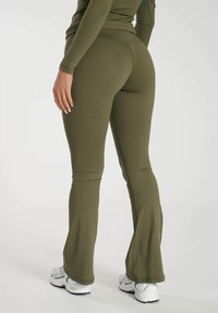 Olivgrön flare leggings gjorda av stretchigt material, med en slät textur, kontrasterande sömmar och matchade med vita träningsskor.