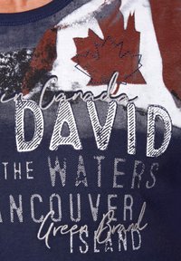 Mornarska majica s grafičnim dizajem koji prikazuje javorov list i tekst: "u Kanadi DAVID the WATERS Vancouver Island Green Brand." Mješavina pamuka.