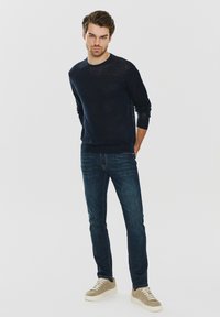 Granatowy sweter z okrągłym dekoltem, lekki dzianinowy, w połączeniu ze slim-fit ciemnoniebieskimi dżinsami. Beżowe skórzane sneakersy z białymi podeszwami.