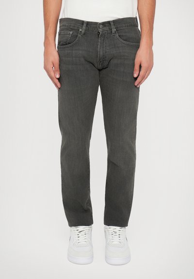 Jeans de mezclilla gris con cinco bolsillos, cierre de botón y corte recto, combinados con zapatillas blancas. Tejido texturizado y sutil desgaste.