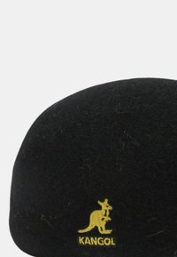 Zwarte vilten baret met een ronde vorm. Heeft een geel Kangol-logo van een kangoeroe, geborduurd aan de zijkant.