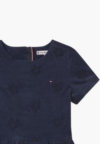 Námořnická modrá šaty pro malé děti s krátkým rukávem, vyšívané hvězdné vzory, malé logo Tommy Hilfiger a nařasený detail sukně.