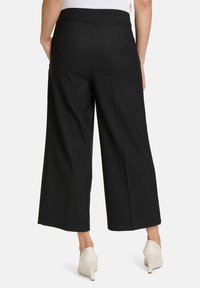Pantalons larges noirs avec une texture lisse, taille élastique et poches arrière, associés à des chaussures à talons hauts crème.