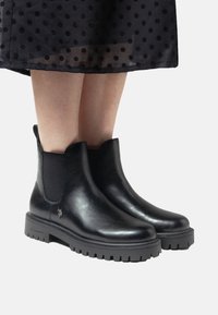 Svarta läderankelbootar med elastiska sidopaneler, gummisula och texturerad sula. Ikonisk logotypdetalj på utsidan.