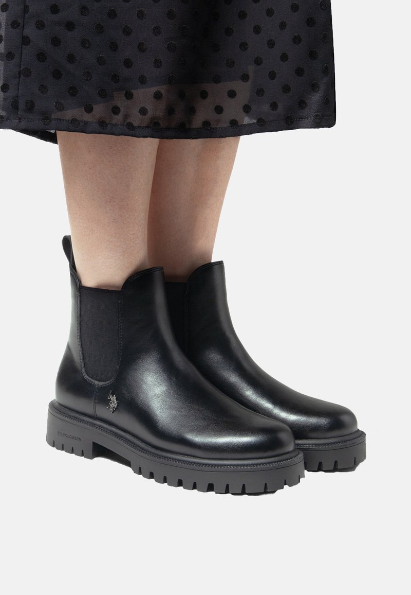 Svarta läderankelbootar med elastiska sidopaneler, gummisula och texturerad sula. Ikonisk logotypdetalj på utsidan.