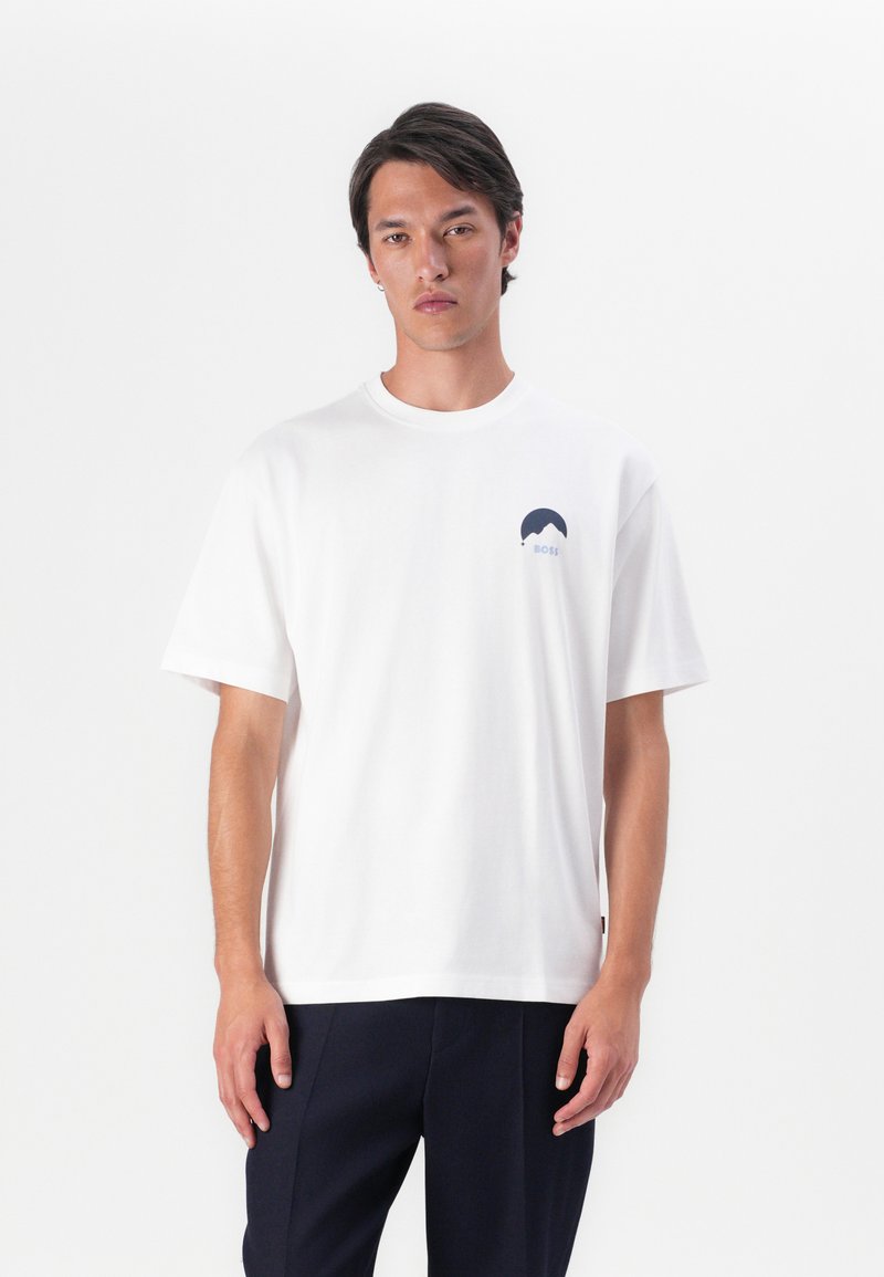 T-shirt en coton blanc avec un logo graphique bleu marine sur la poitrine. Coupe décontractée avec des manches courtes et un col rond.