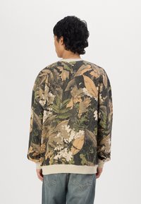 Felpa con motivo camouflage e maniche lunghe, caratterizzata da foglie in tonalità terrose di verde, marrone e crema. Collo e orlo a coste, materiale in misto cotone.
