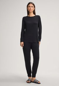Zwarte langemouwen top met gestructureerde manchetten, gecombineerd met zwarte broek met elastische uiteinden. Draag met zwarte slide sandalen waarop het logo te zien is.