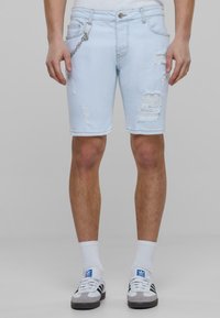 Pantalones cortos de mezclilla de color azul claro con detalles desgastados, cinco bolsillos y un acento de cadena en la cintura. Diseño de ajuste estándar y longitud hasta la rodilla.