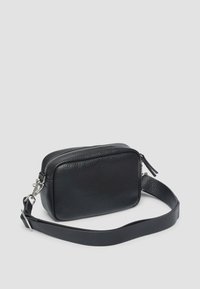 Zwarte leren crossbody tas met een rechthoekige vorm, textuur oppervlak, ritsluiting en een verstelbare schouderband. Voorzien van zilveren hardware accenten.
