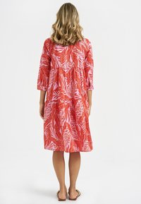 Red and pink floral printed dress, with three-quarter sleeves, gathered waist, and knee-length hem. Made of lightweight fabric.